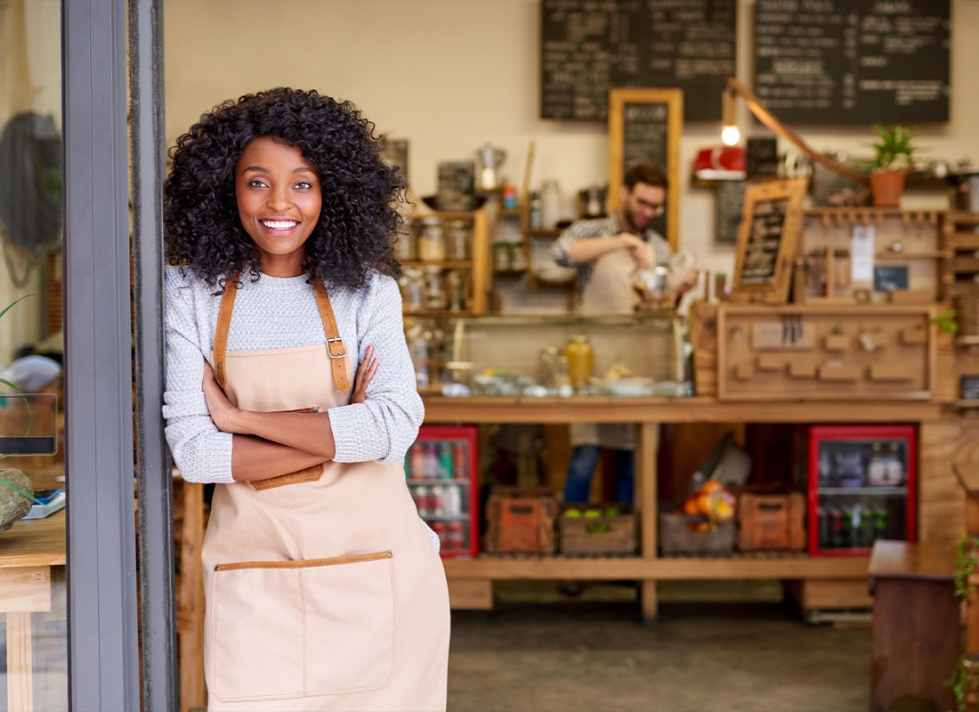 Business Insurance - Barista Standing Welcomingly at a Cafe Door While Smiling