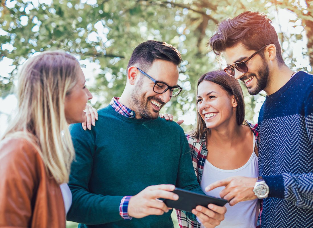 Read Our Reviews - Image of Four Happy Smiling Young Friends Walking Outdoors in the Park While Holding a Tablet